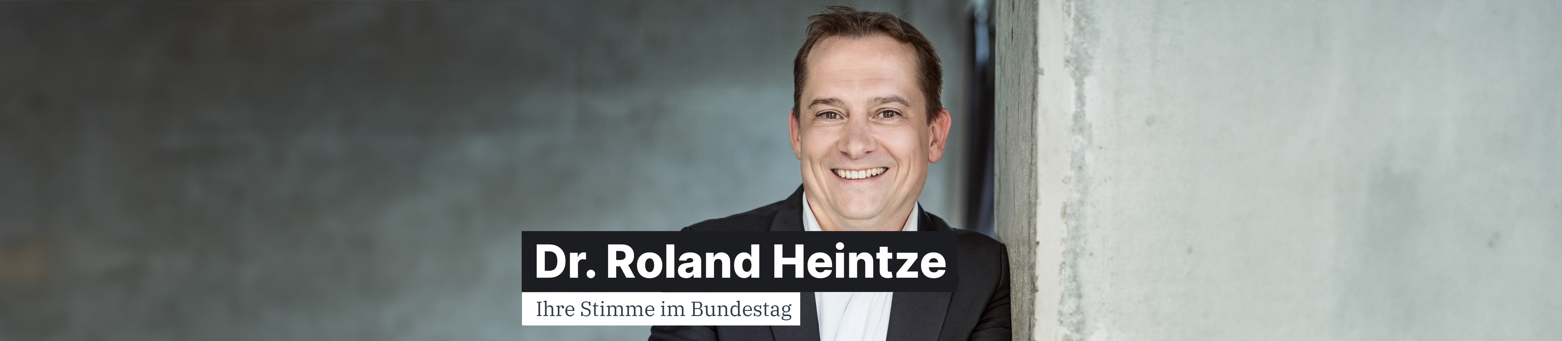 Dr. Roland Heintze lehnt an einer Säule und schaut den Betracher freundlich an.